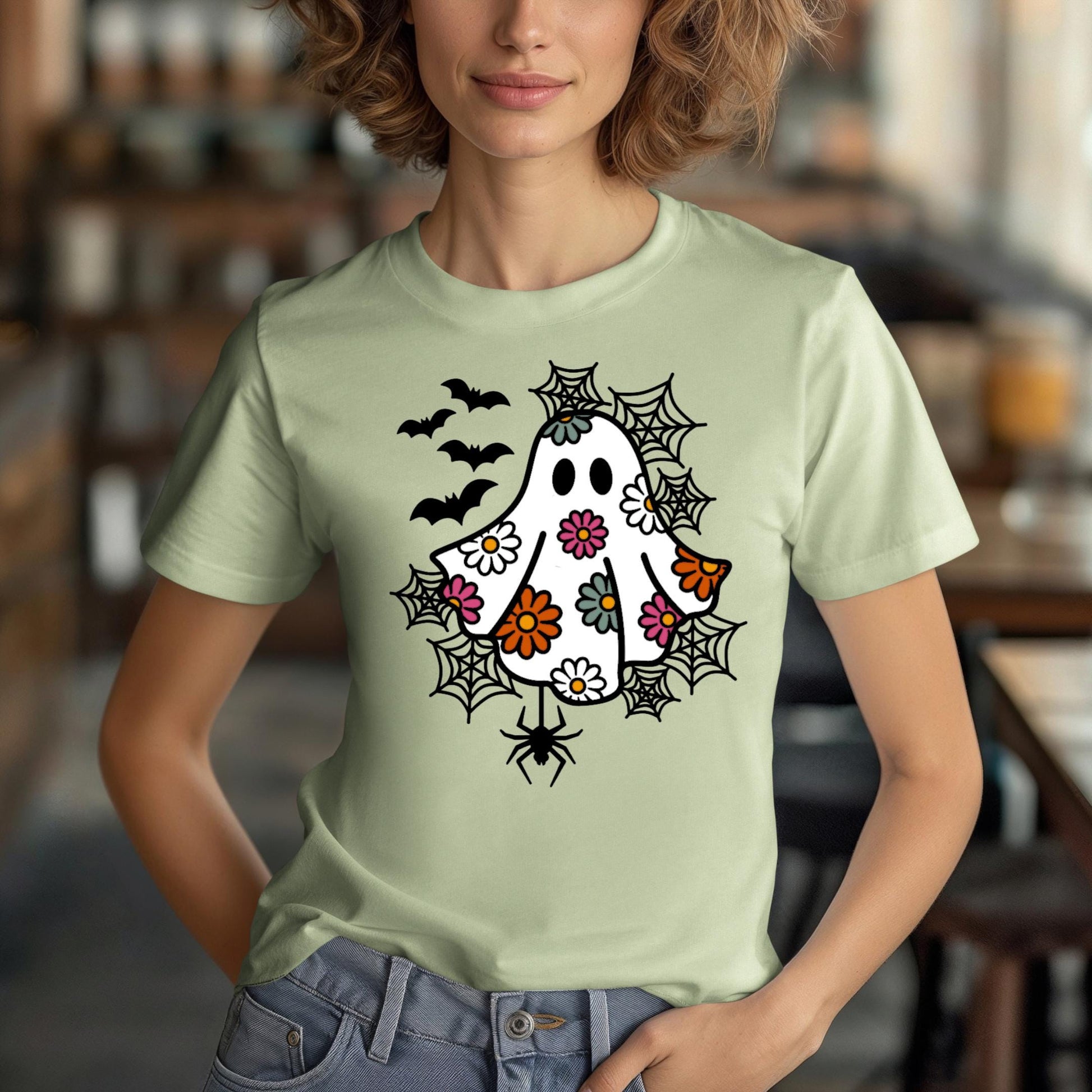 A woman wearing a green t-shirt with a whimsical design featuring a ghost, bats, and spiders on it.