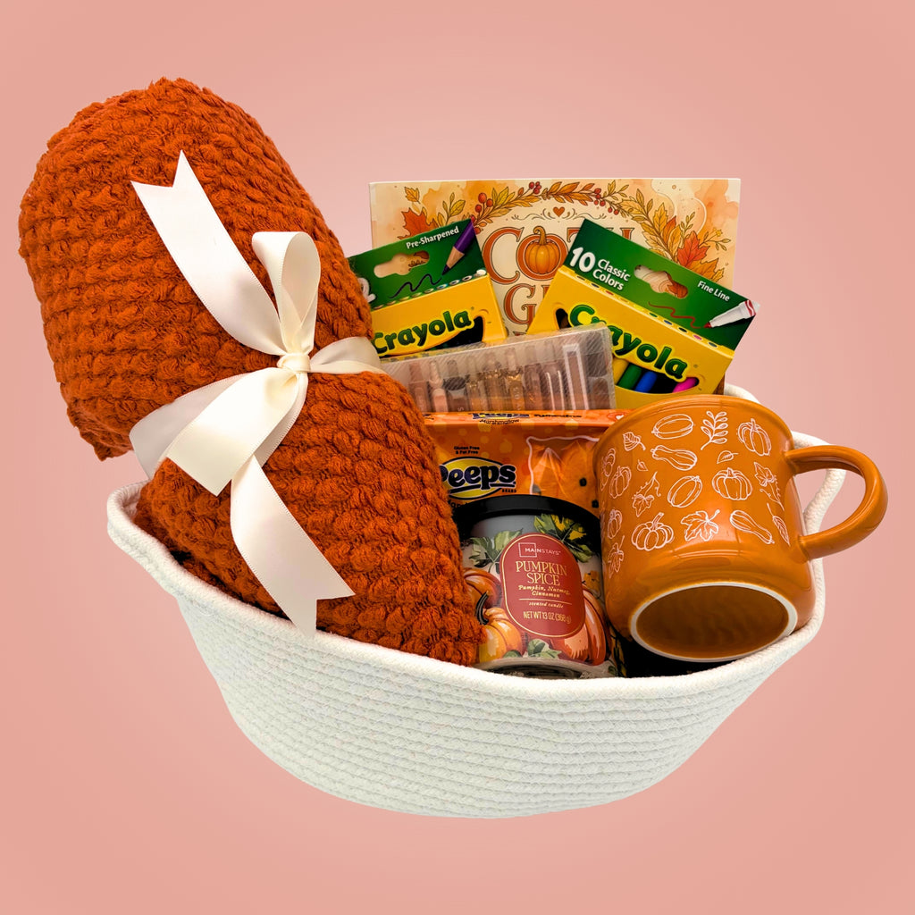 Fall coloring gift basket with an orange knit throw blanket tied with a cream bow, coloring book, pumpkin mug, candle, and markers