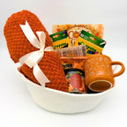 Cream rope fall gift basket with a cozy orange throw blanket, coloring book, markers, pumpkin mug, and candle on white