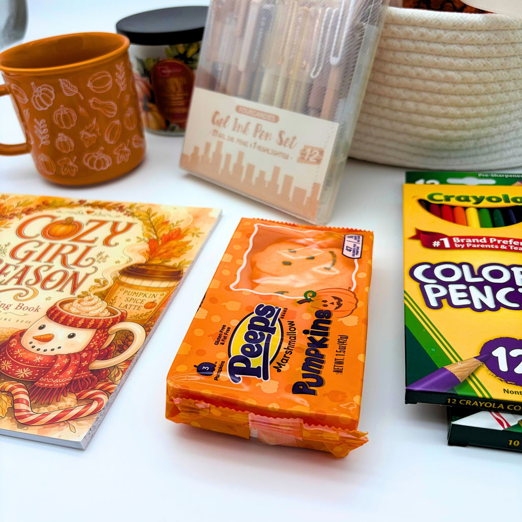 Marshmallow pumpkin treats beside the Cozy Girl Season coloring book and colored pencils, with the mug, candle, and basket behind