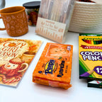 Marshmallow pumpkin treats beside the Cozy Girl Season coloring book and colored pencils, with the mug, candle, and basket behind
