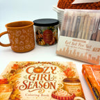 Burnt orange mug with white pumpkin and gourd line art beside a pumpkin spice candle, neutral gel pen set, and the coloring book