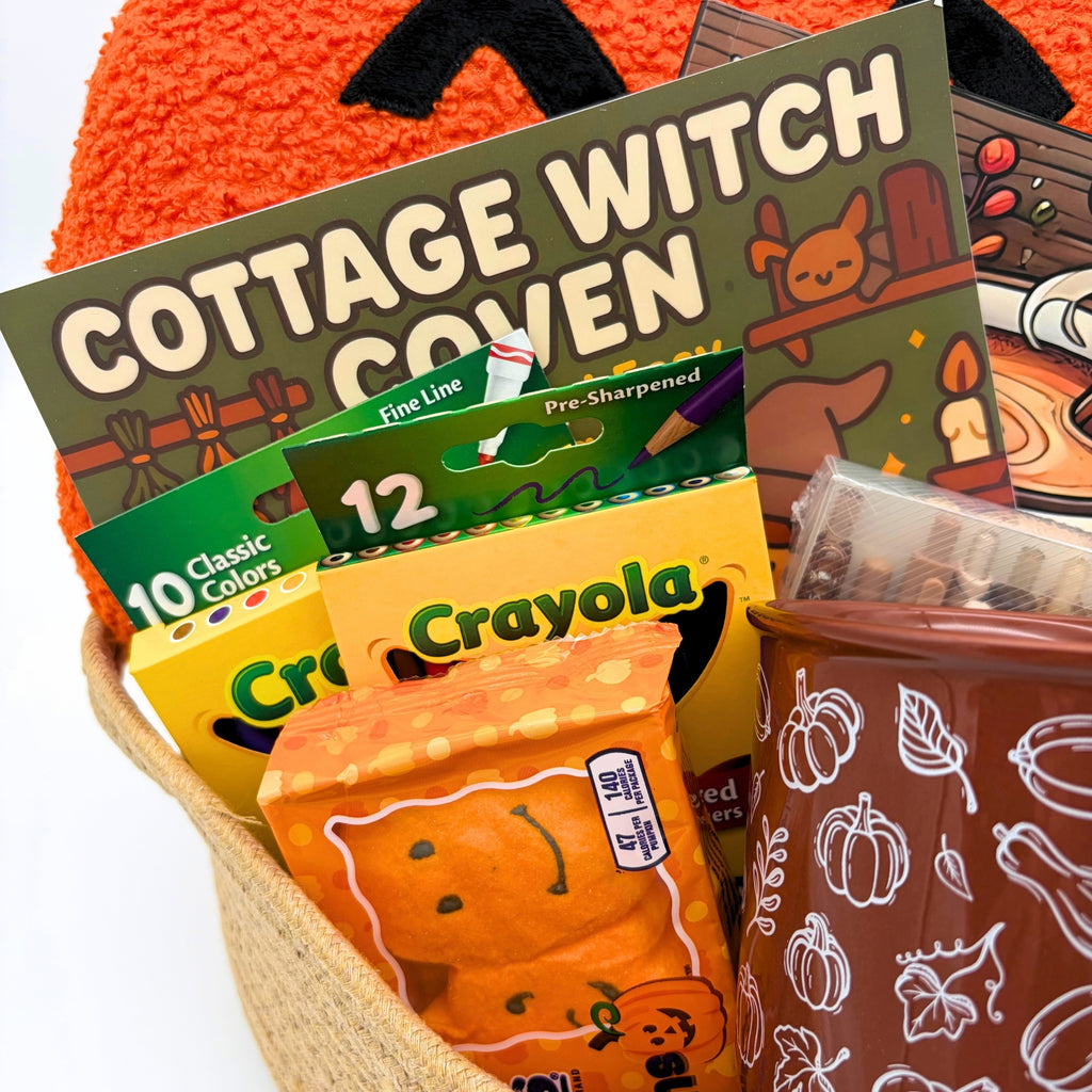 Close-up of the Cottage Witch Coven coloring book, colored pencils, markers, marshmallow pumpkins, and a brown mug with white gourd art