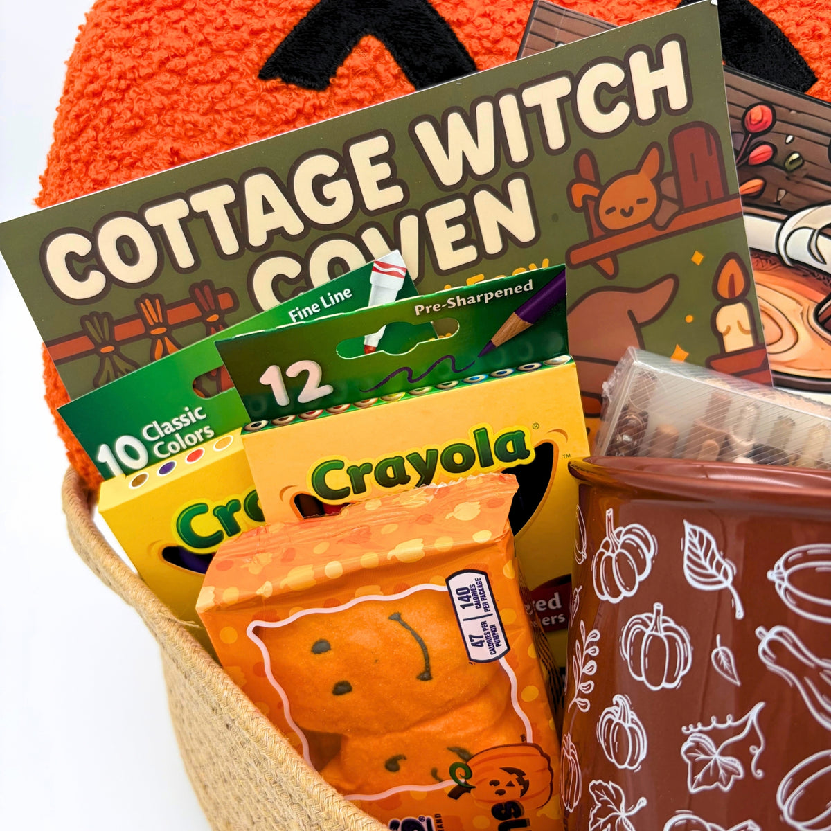 Close-up of the Cottage Witch Coven coloring book, colored pencils, markers, marshmallow pumpkins, and a brown mug with white gourd art