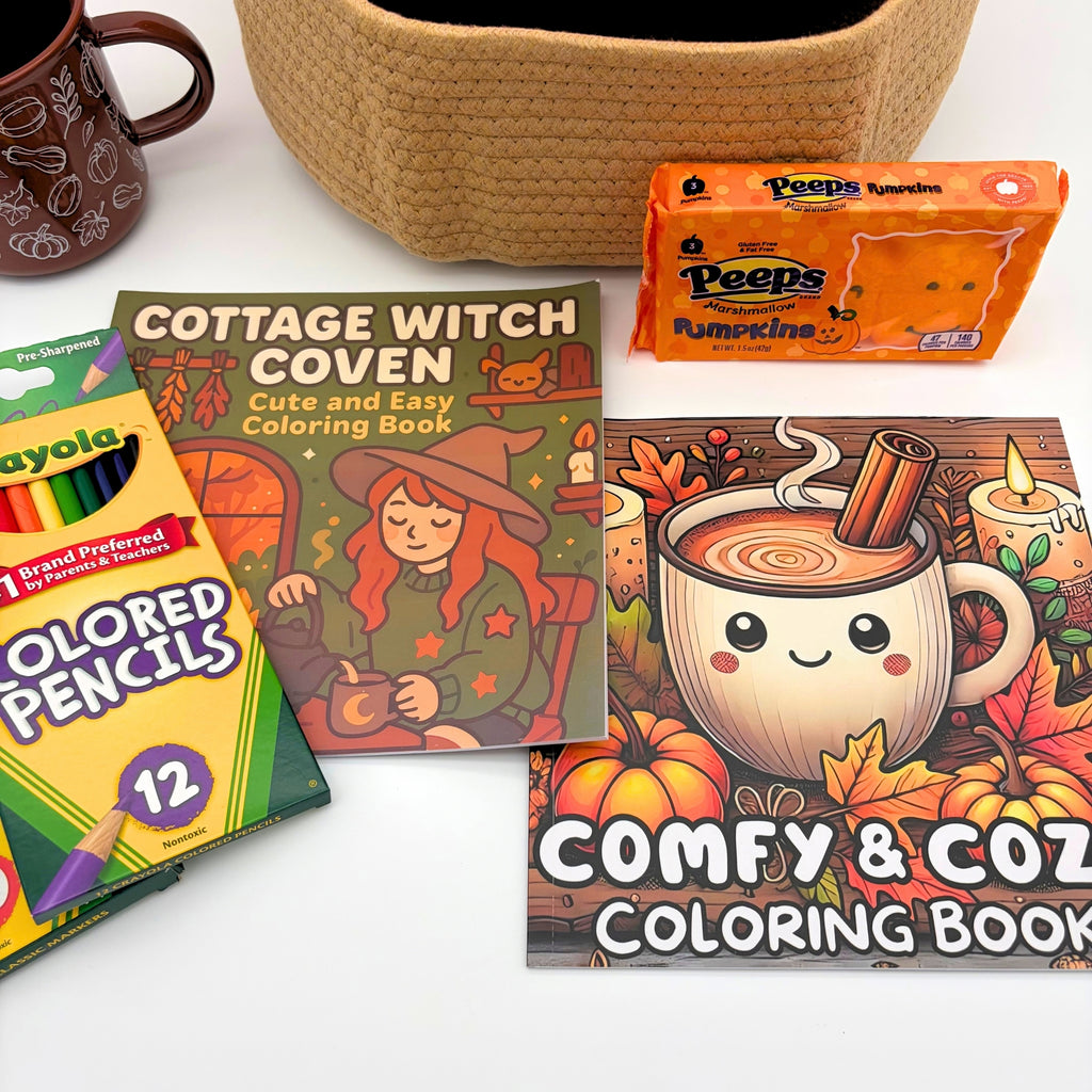Cottage Witch Coven and Comfy & Cozy coloring book covers beside colored pencils, markers, and marshmallow pumpkins on white