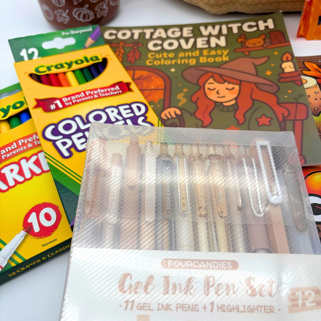 Close-up of a 12-piece gel pen set in warm neutral tones in front of colored pencils, markers, and the witch coloring book