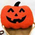 Close-up of an orange boucle jack-o'-lantern pillow with a black appliqué face and stem sitting on top of a tan rope basket