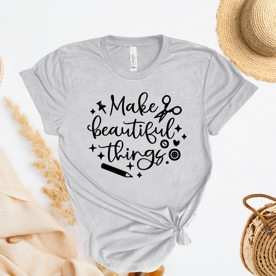 Gray t-shirt with 'Make beautiful things' text with scissors, buttons, and a pencil on a light background