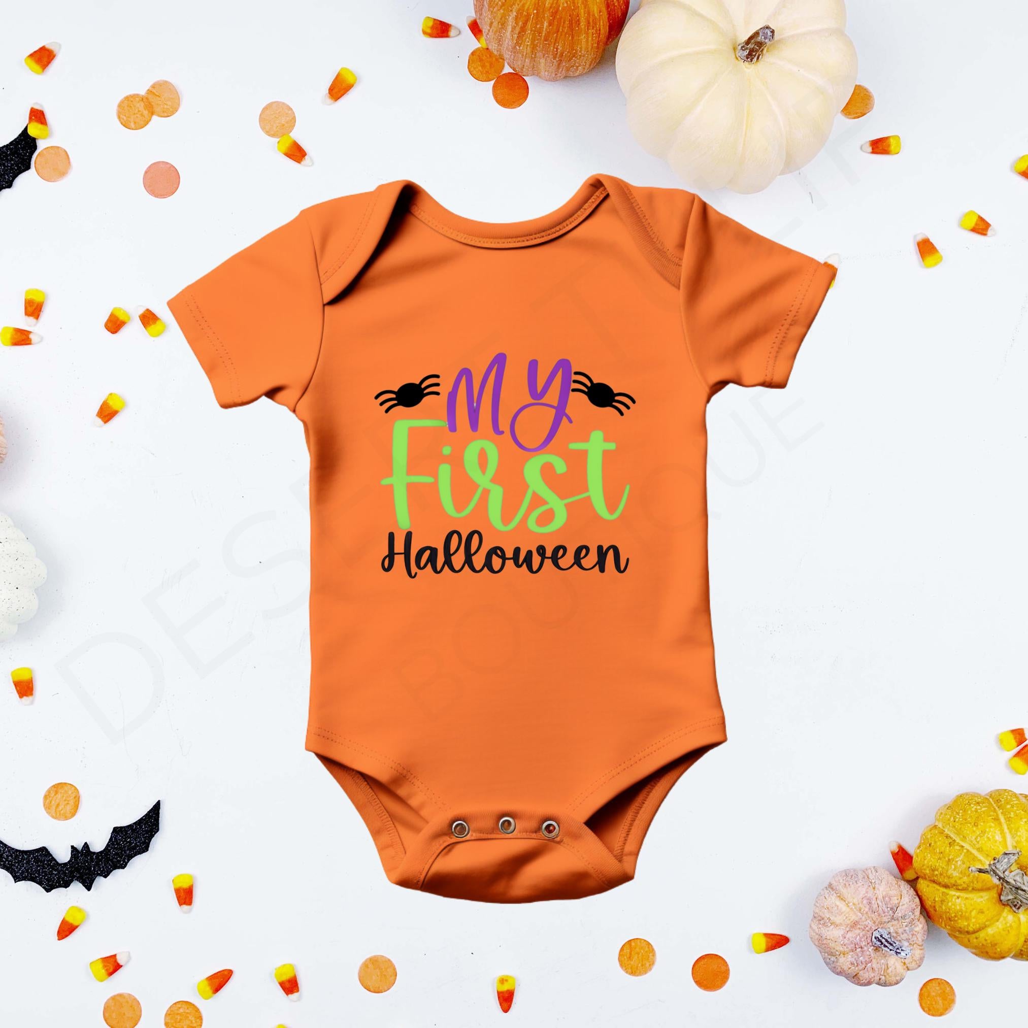 "My First Halloween" in purple, green, and black lettering, flanked by two black spiders on an orange baby bodysuit