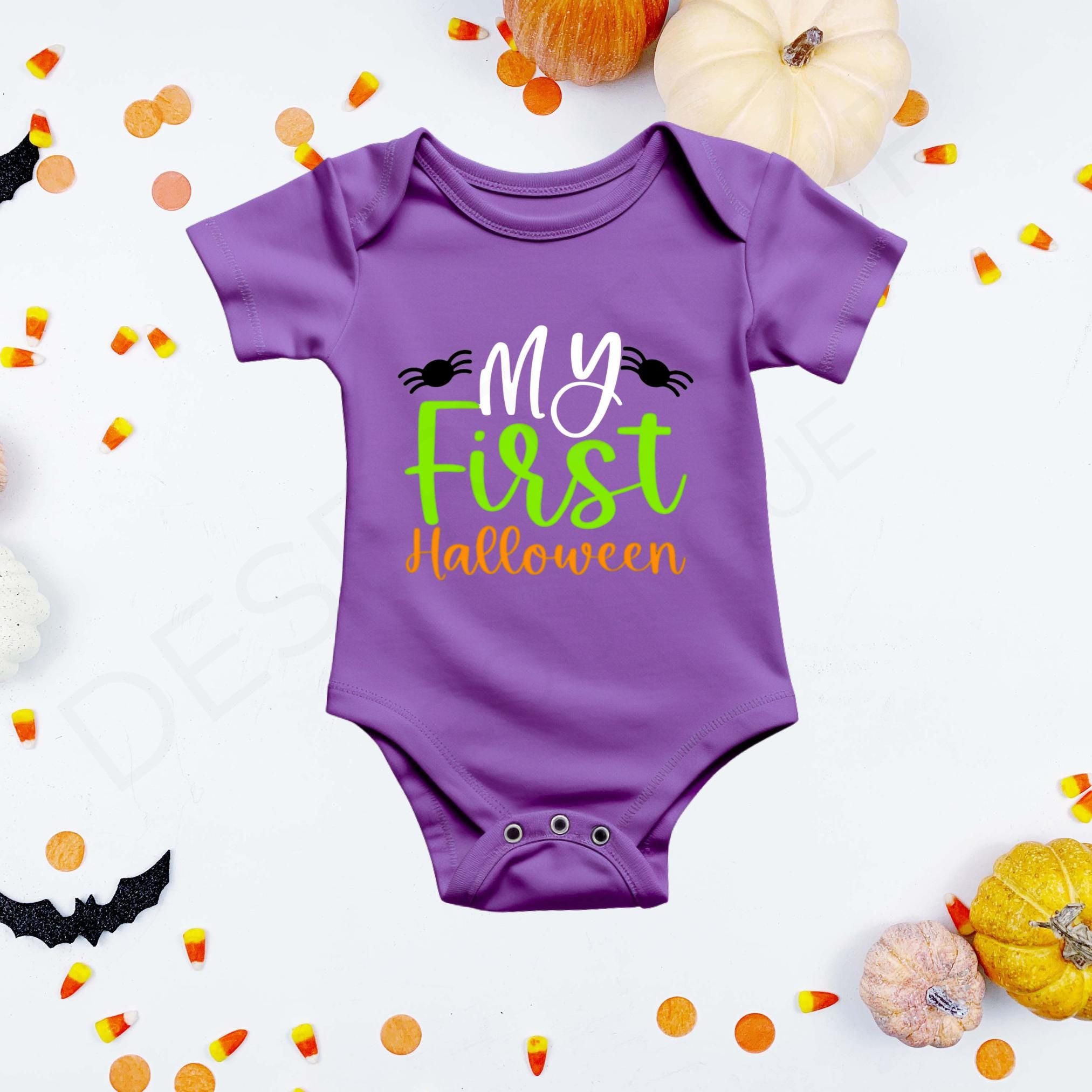 "My First Halloween" in white, green, and orange lettering flanked by two black spiders on a purple baby bodysuit