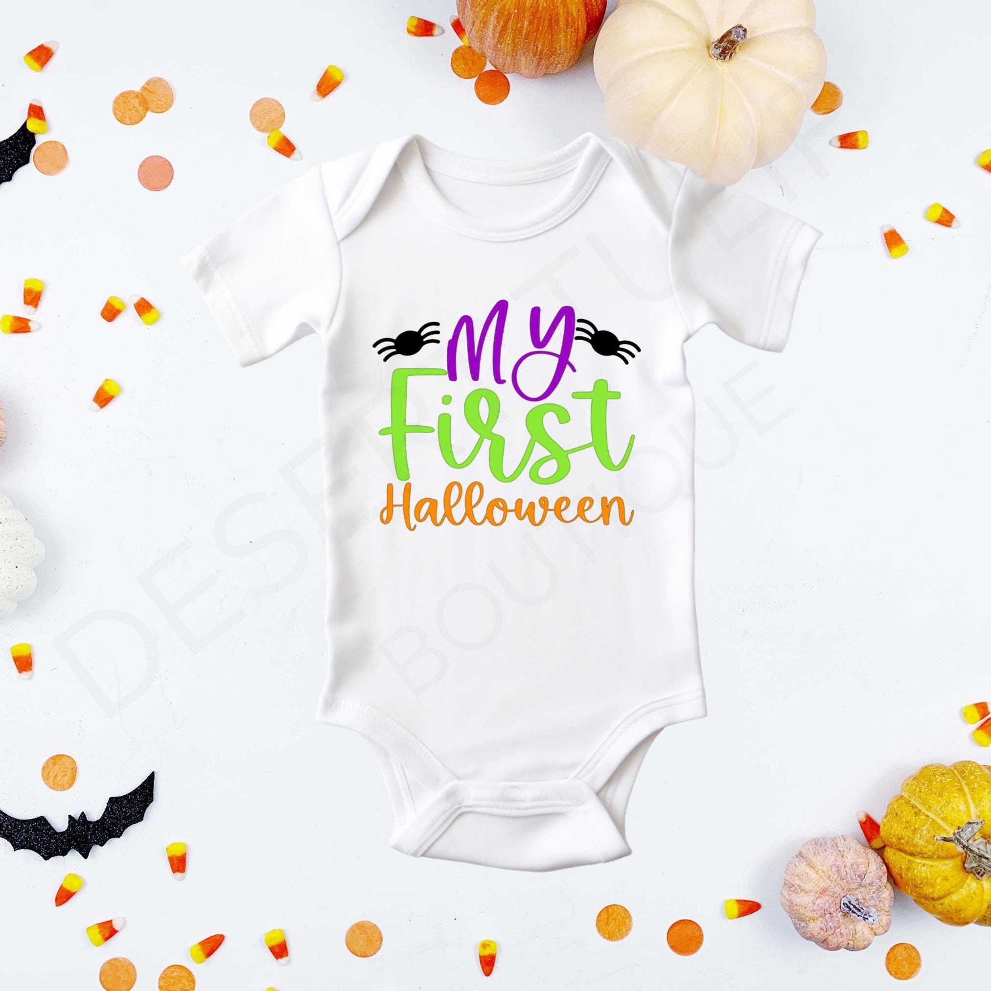 "My First Halloween" in purple, green, and orange lettering flanked by two black spiders on a white baby bodysuit