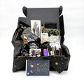 Open black gift box with celestial tissue holding the mystical witchy gift box contents, with a gold star and moon greeting card in front