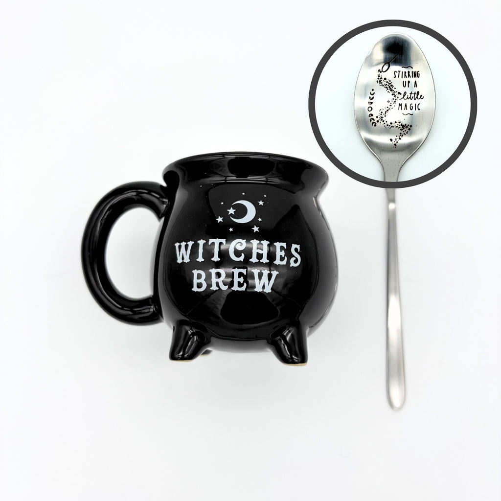 Witches brew cauldron mug in black with a crescent moon, shown with the silver spoon stamped stirring up a little magic