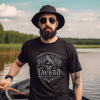 Man wearing an 'Old Crow Tavern' black t-shirt with a vintage tavern design, standing by a lake.