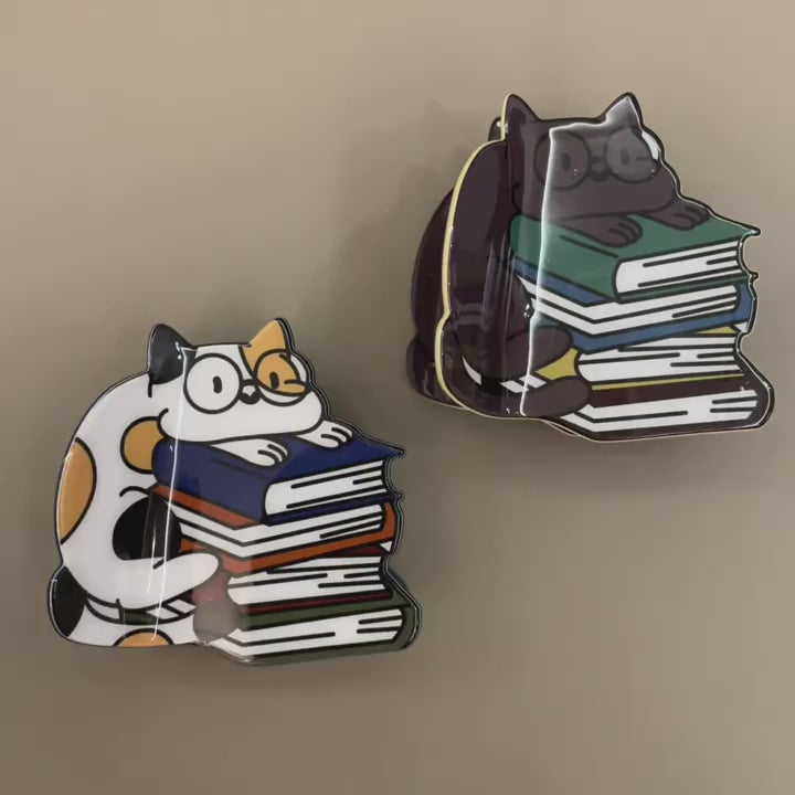 A person picking up, moving and opening and closing hair clips that look like a cat hugging a stack of books.