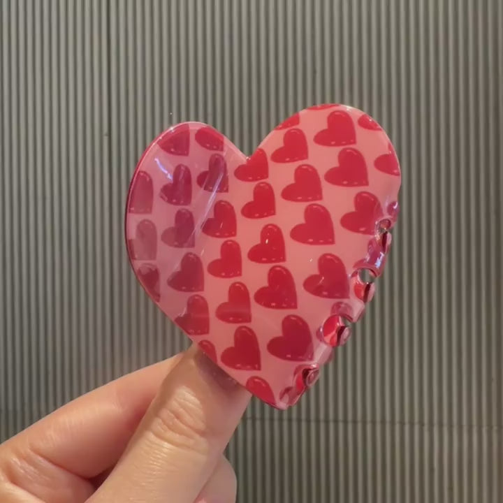 Video of person rotating, opening, and closing a hear shaped hair claw clip with glossy red hearts pattern.