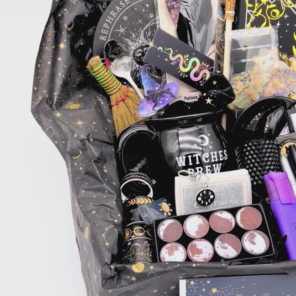 Slow pan across the open mystical witchy gift box showing the crystal wand, pendulum board, moon phase journal, pen collection and witches brew mug