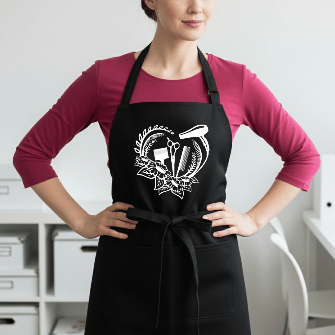 Black professional stylist apron with white heart-shaped floral wreath and salon tools design worn by female stylist