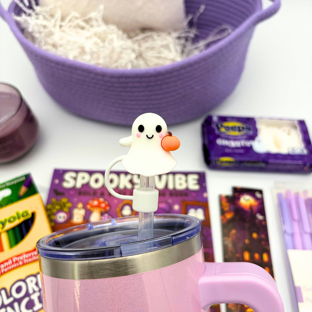 Close-up of a white ghost straw topper with pink cheeks holding a tiny orange pumpkin on a lilac tumbler lid