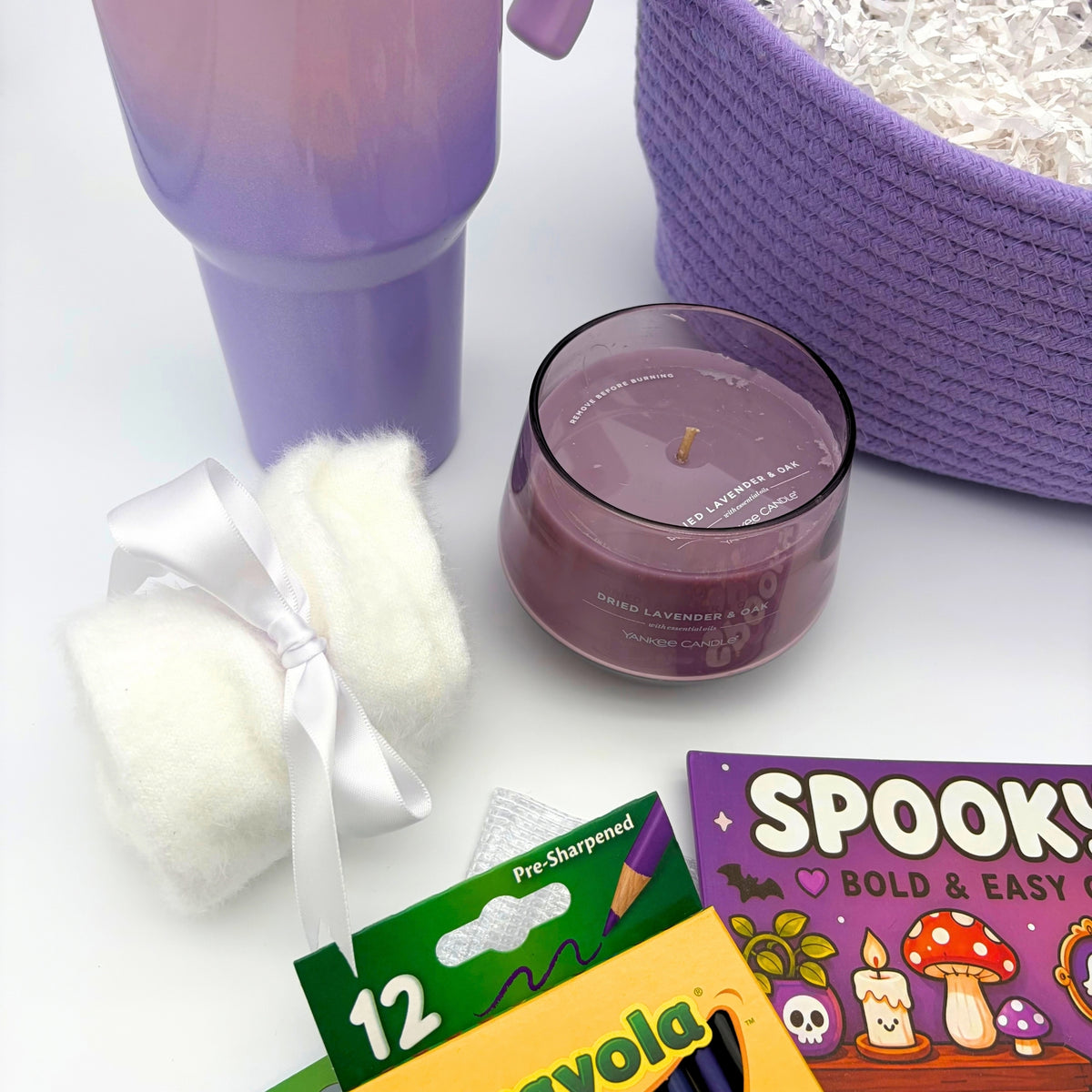 Fuzzy white socks tied with a satin bow next to a dried lavender and oak candle in a tinted glass jar, viewed from above