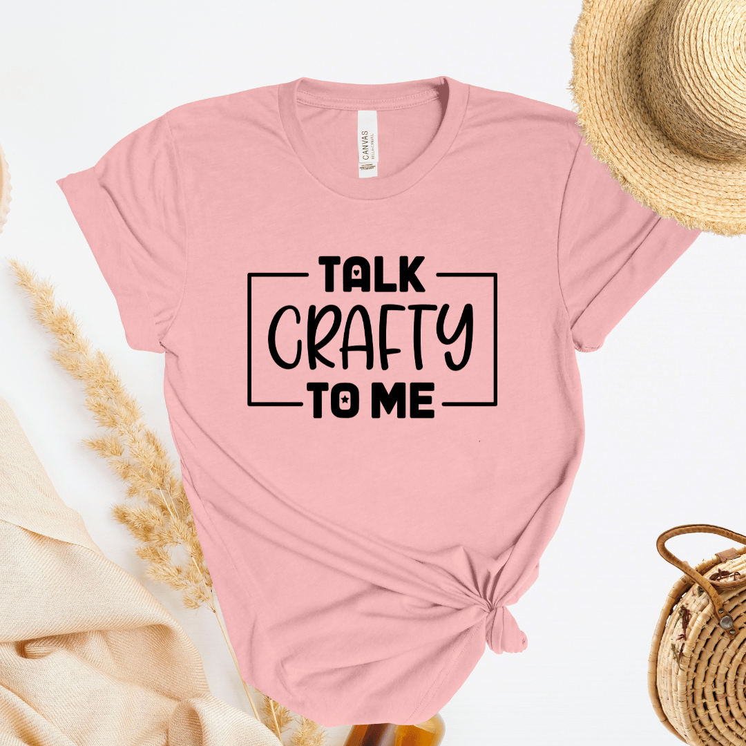 Light pink t-shirt with 'Talk Crafty to Me' text, straw hat, and bag on a white background