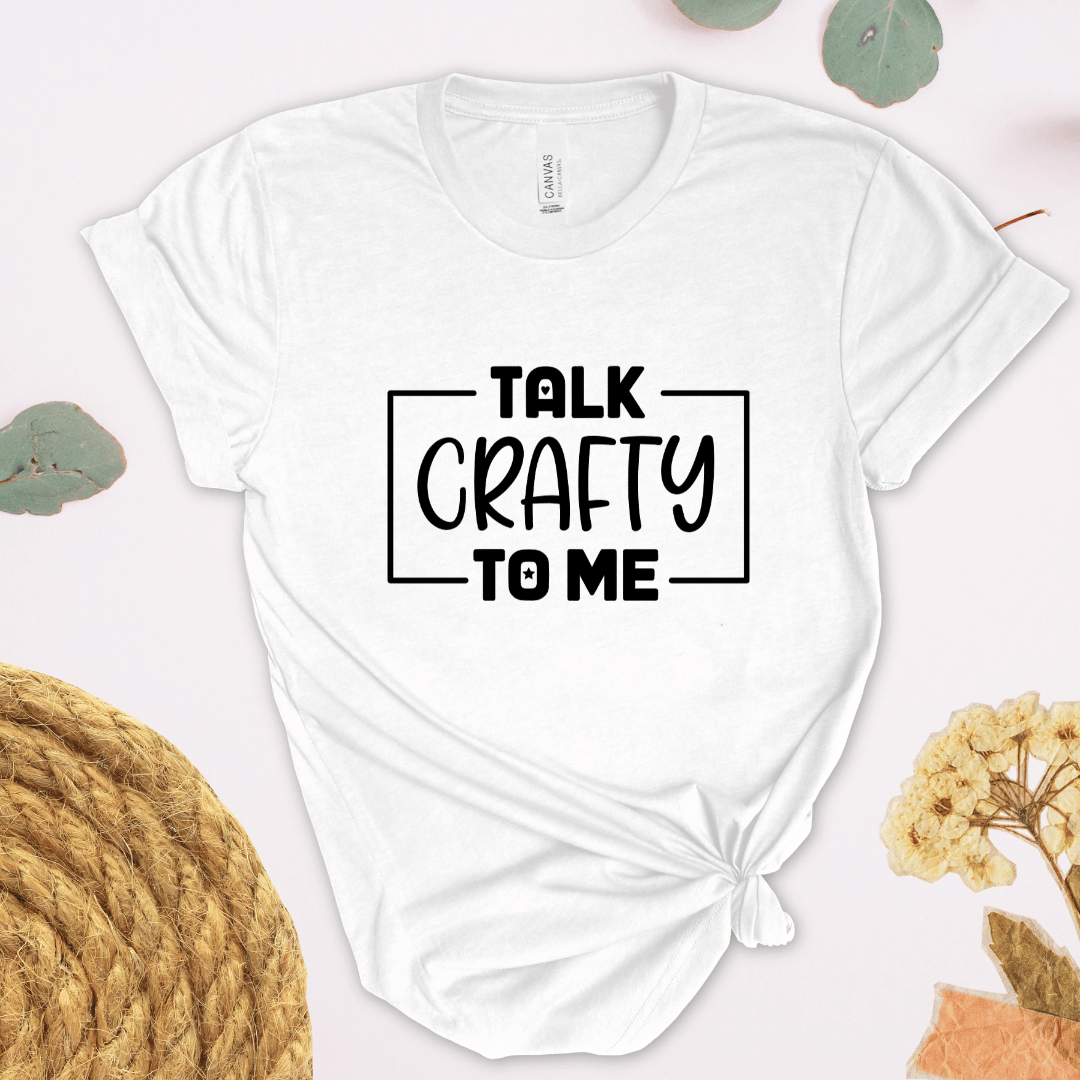 White t-shirt with 'Talk Crafty to Me' text on a light background with decorative elements.