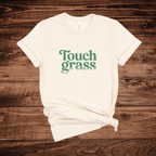 Touch Grass funny meme t-shirt with retro serif font and grass blade lettering on a cream shirt