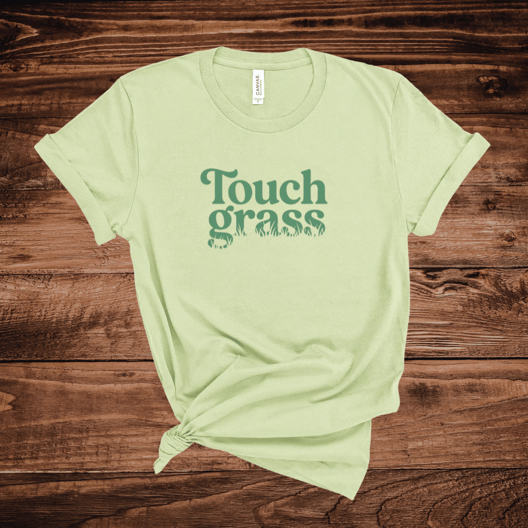 Touch Grass funny outdoor humor t-shirt with retro serif font and grass blade lettering on a light green shirt