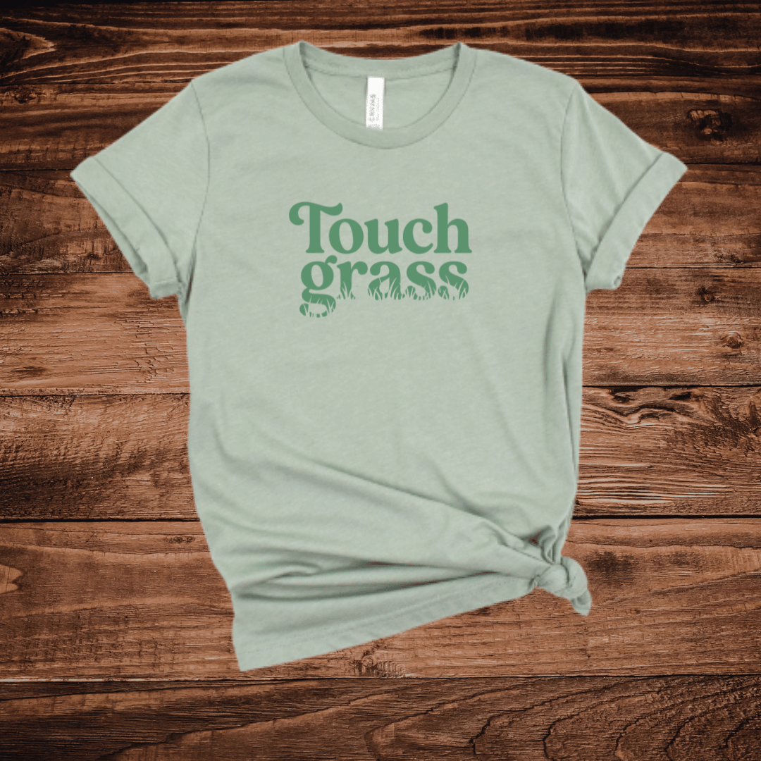 Touch Grass funny nature lover t-shirt with retro serif font and grass blade lettering on a sage green shirt