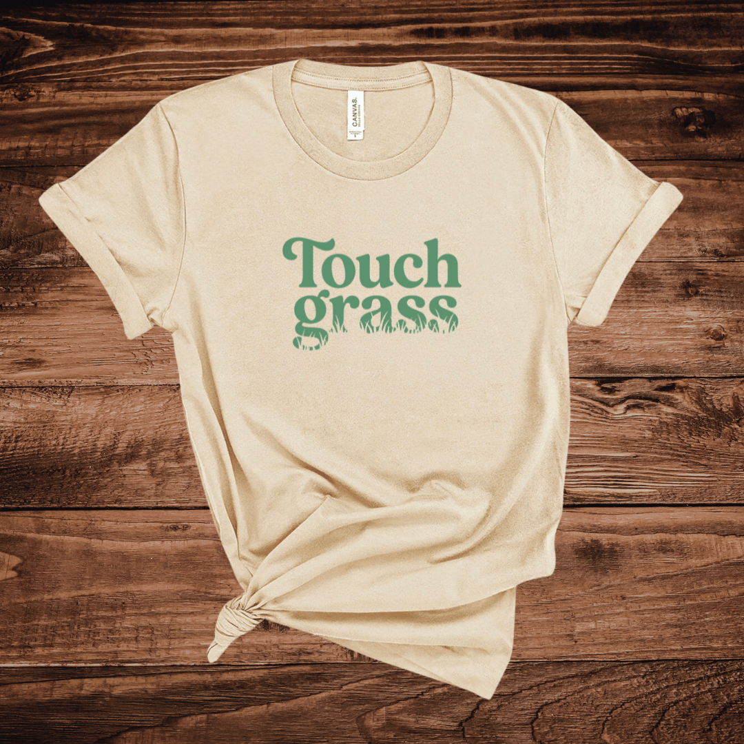 Touch Grass funny meme t-shirt with retro serif font and grass blade lettering on a tan shirt